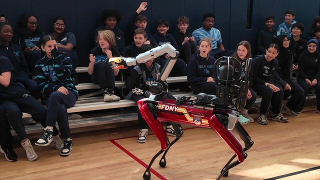Students sit on bleachers looking at a robotic FDNY dog. 