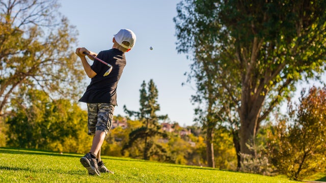 Young Boy Golfer Teeing Off During Sunset 