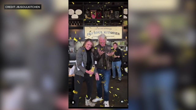 Jon Bon Jovi and his wife stand in a JBJ Soul Kitchen while gold confetti falls. 